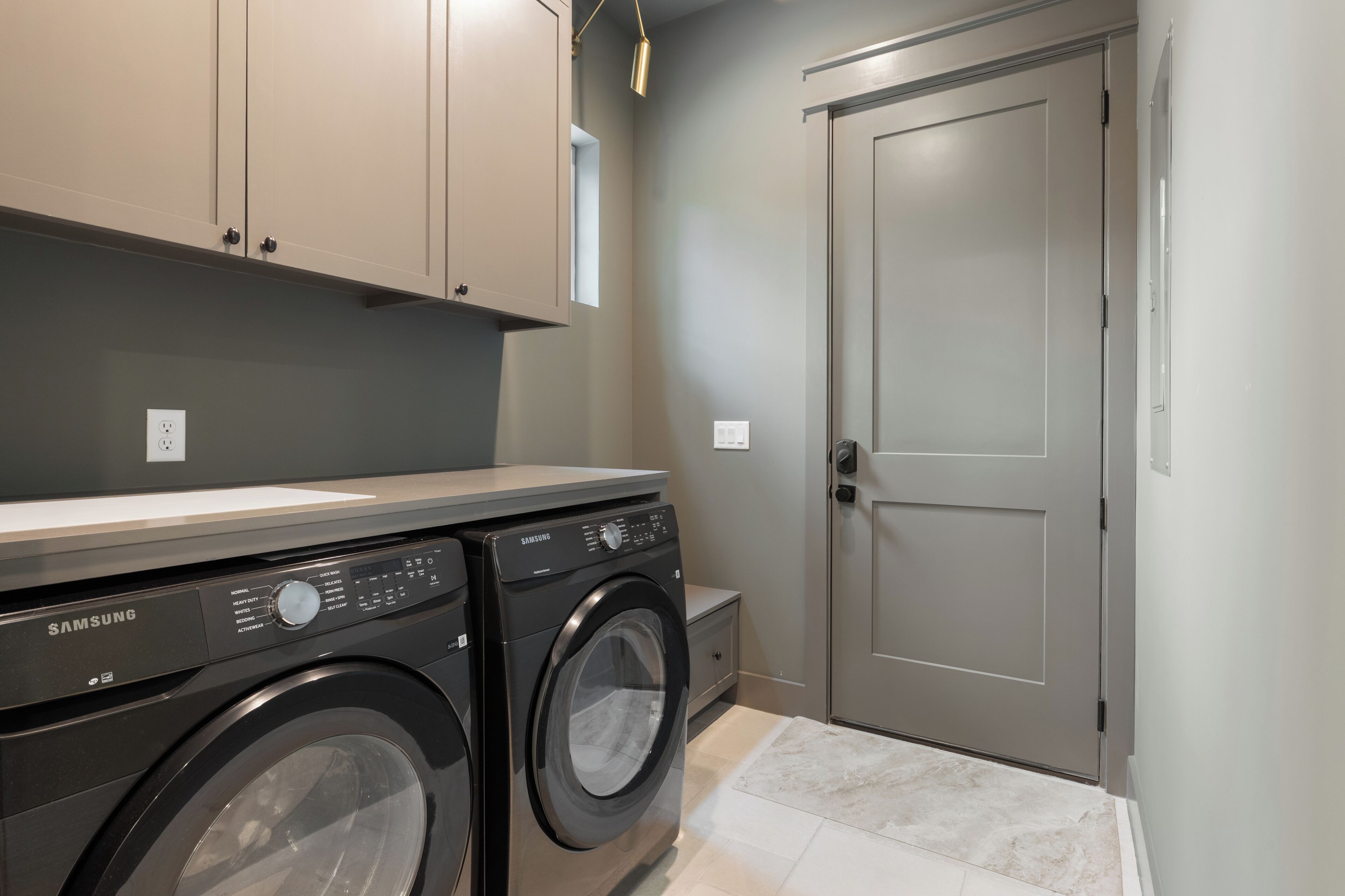 A laundry area with a Samsung washer and dryer, a grey door, and a small window.