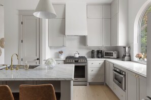 A modern kitchen with white cabinetry, a marble countertop, stainless steel appliances, and a large window. - Tremendous 9-bedroom Luxury Compound - Two Pools & Two Houses (Austin)