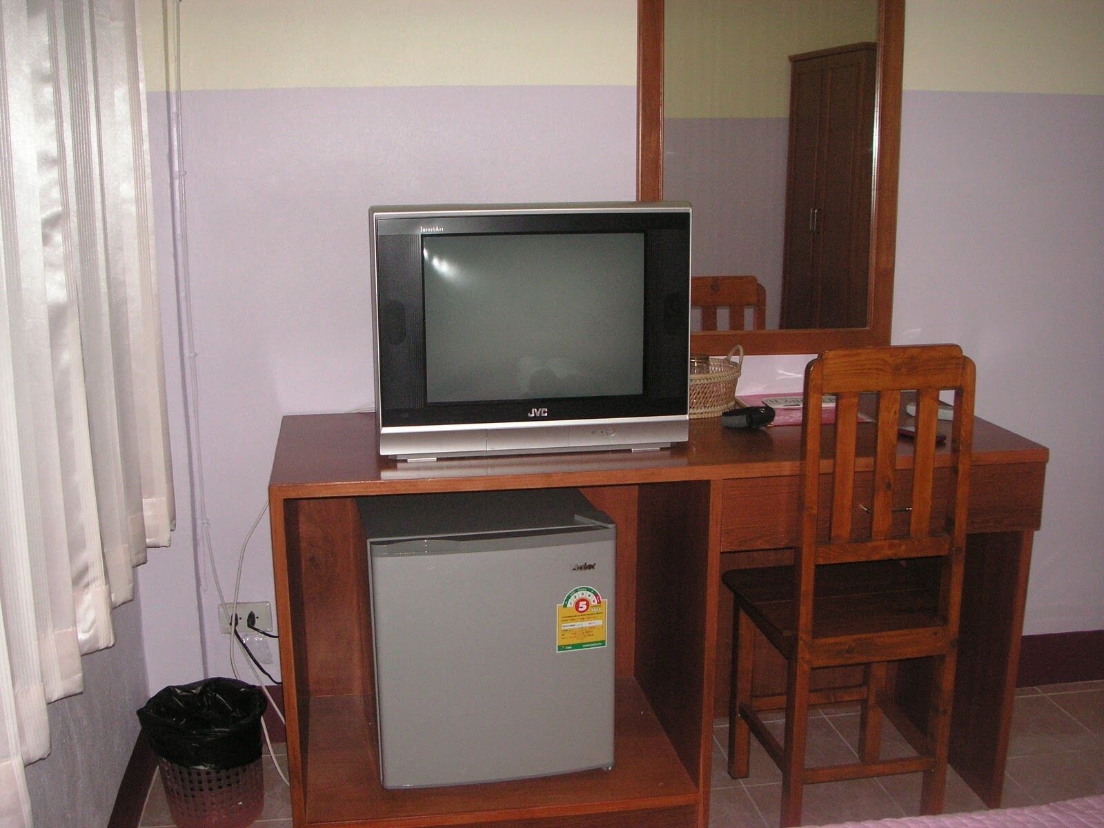 Un escritorio de madera con un televisor, un refrigerador pequeño y una silla.