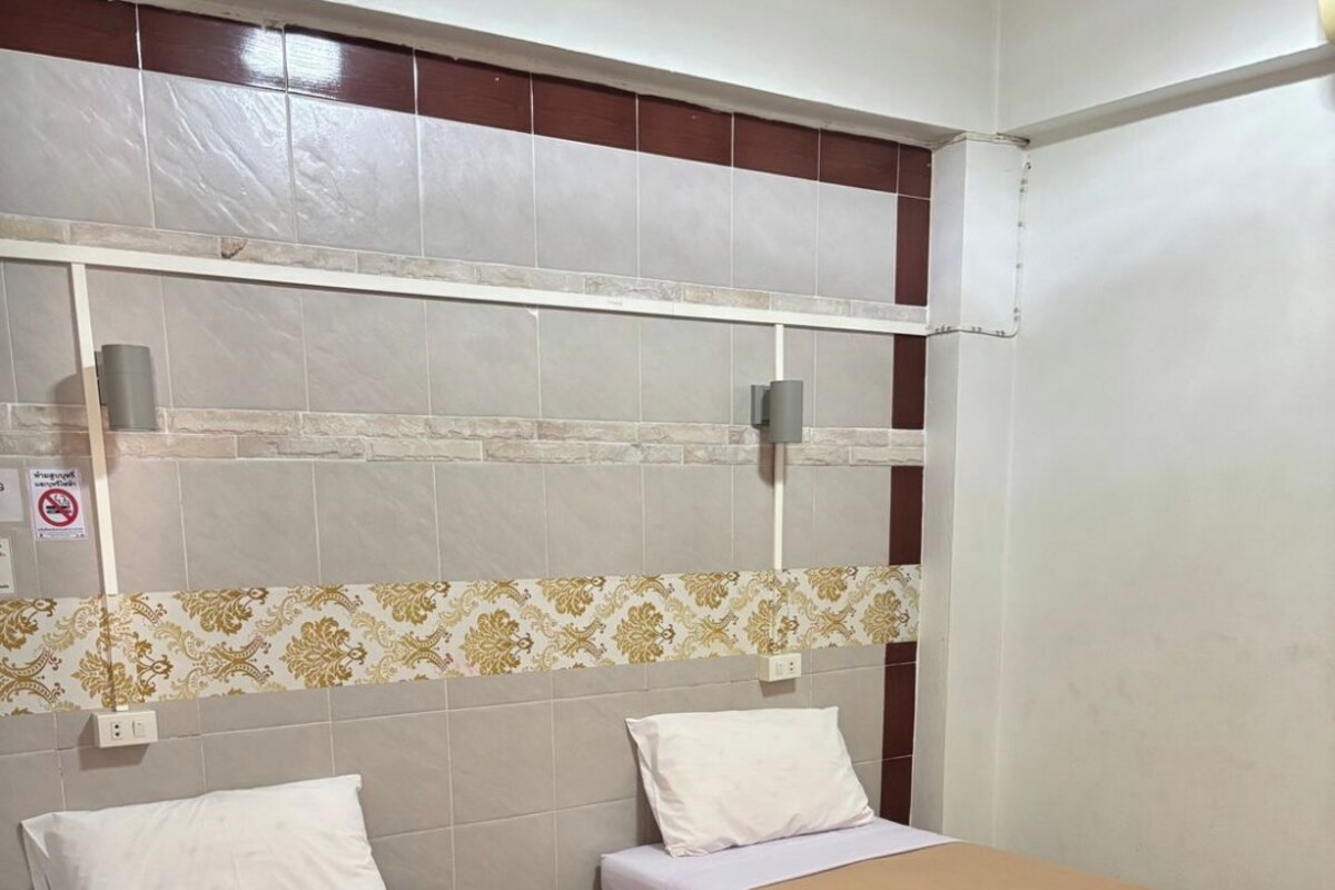 Habitación de hotel con dos camas, pared de azulejos, un borde estampado y una pared blanca con un cartel de no fumar.
