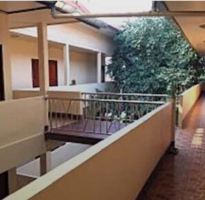 Um corredor com corrimão de metal, escada e uma planta verde.