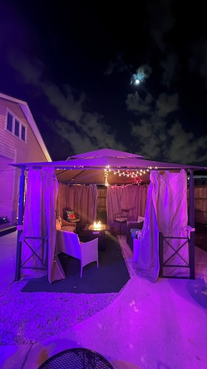 A covered outdoor seating area with a table and chairs, under a canopy with draped fabric. - Historic Double Shotgun Home in Spanish Town, Downtown Baton Rouge (Baton Rouge)