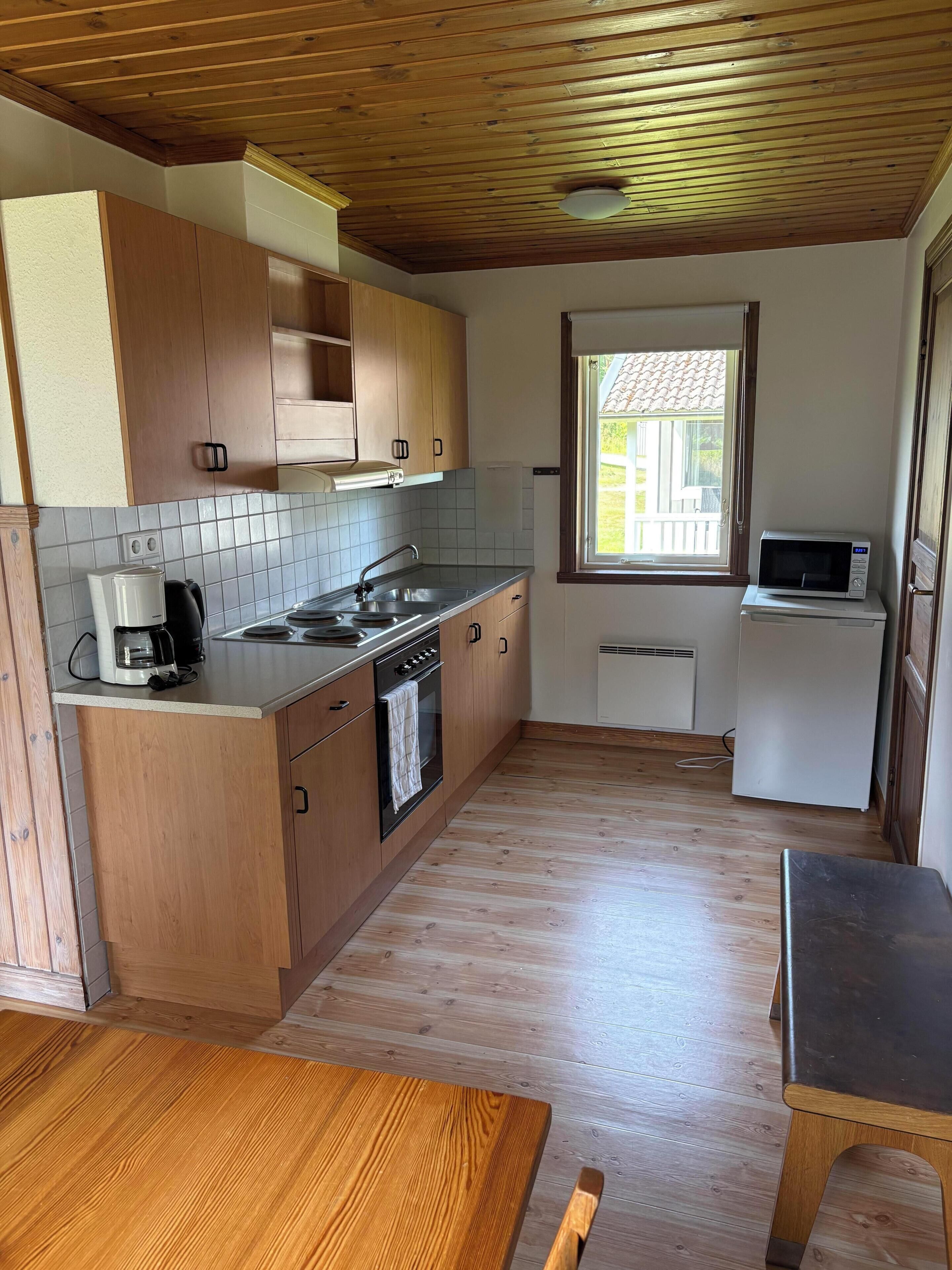 A compact kitchen with wooden cabinets, a built-in oven, a coffee maker, and a microwave.