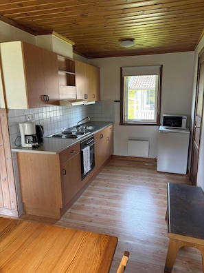A compact kitchen with wooden cabinets, a built-in oven, a coffee maker, and a microwave. - Björnbyn Stugby (Värmlands län)