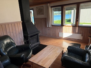 Una habitación con chimenea, sillones de cuero, una mesa de madera y ventanas con vistas al agua.