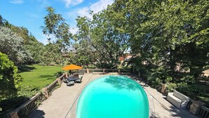 A swimming pool with a surrounding deck, a patio with outdoor furniture, and a view of a grassy yard.