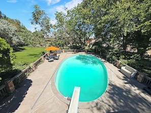 A swimming pool with a surrounding deck, a patio with outdoor furniture, and a view of a grassy yard.