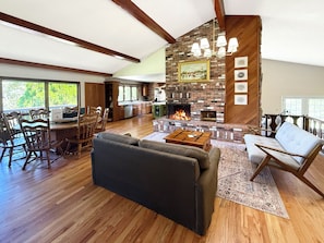 A spacious living room with a fireplace, wooden flooring, and a dining area with wooden furniture.