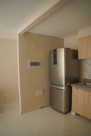 A kitchen with a stainless steel refrigerator, wooden cabinets, and a tiled floor.