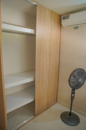 A room with a wooden wardrobe, a standing fan, and a wall-mounted air conditioner.