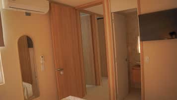 A bedroom with a bed, a bedside table, a mirror, a wardrobe, and an air conditioning unit.