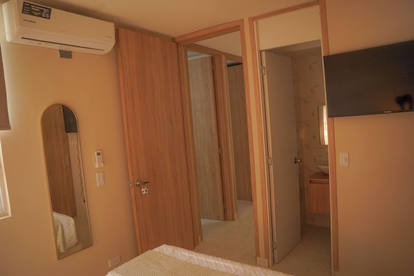 A bedroom with a bed, a bedside table, a mirror, a wardrobe, and an air conditioning unit.