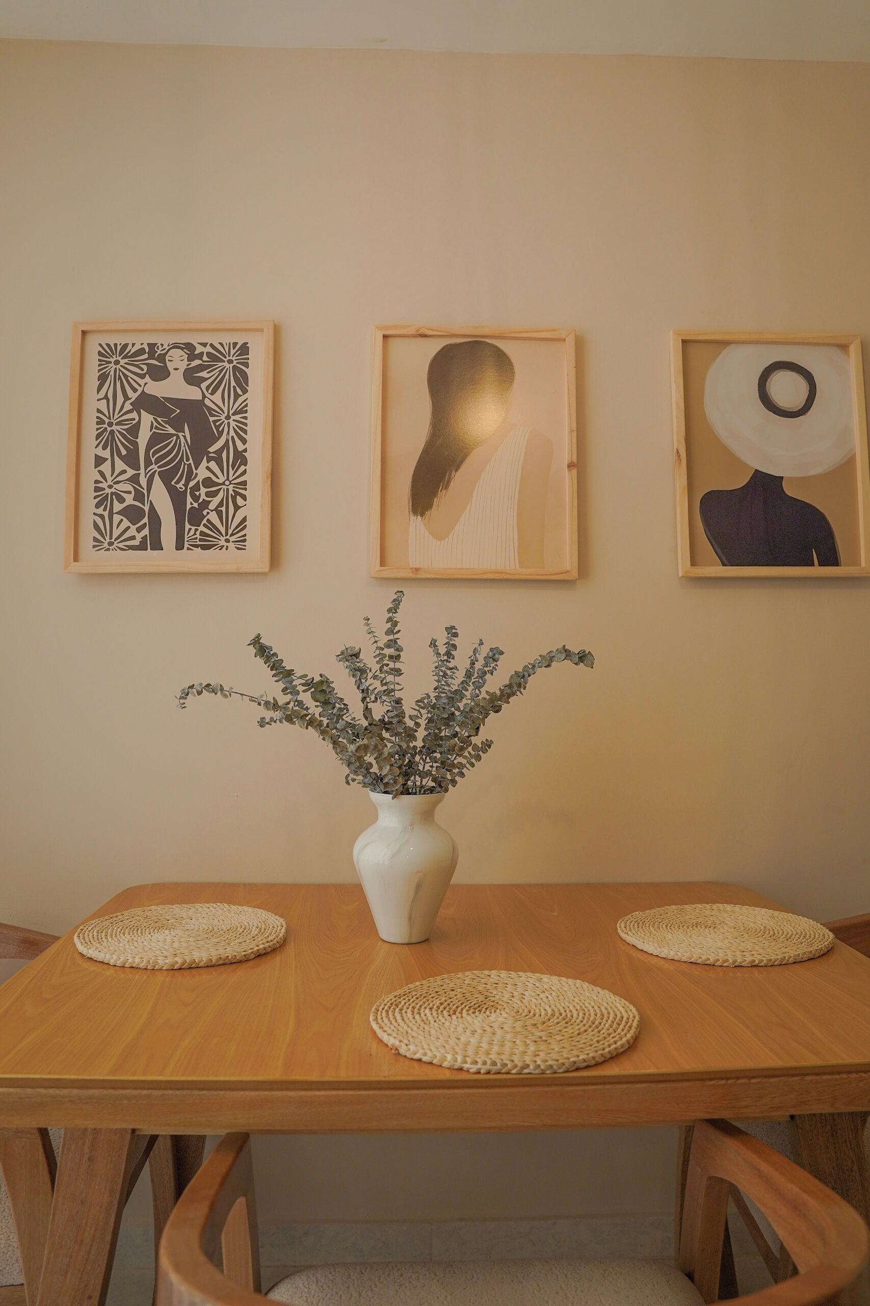 A dining table with a white vase and three woven placemats.
