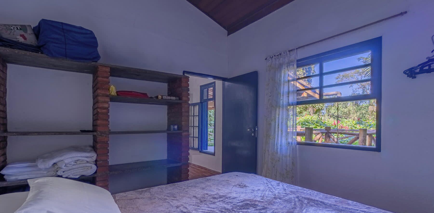 Una habitación con literas, una cama individual, un ventanal con vista a follaje y una puerta que da al exterior.