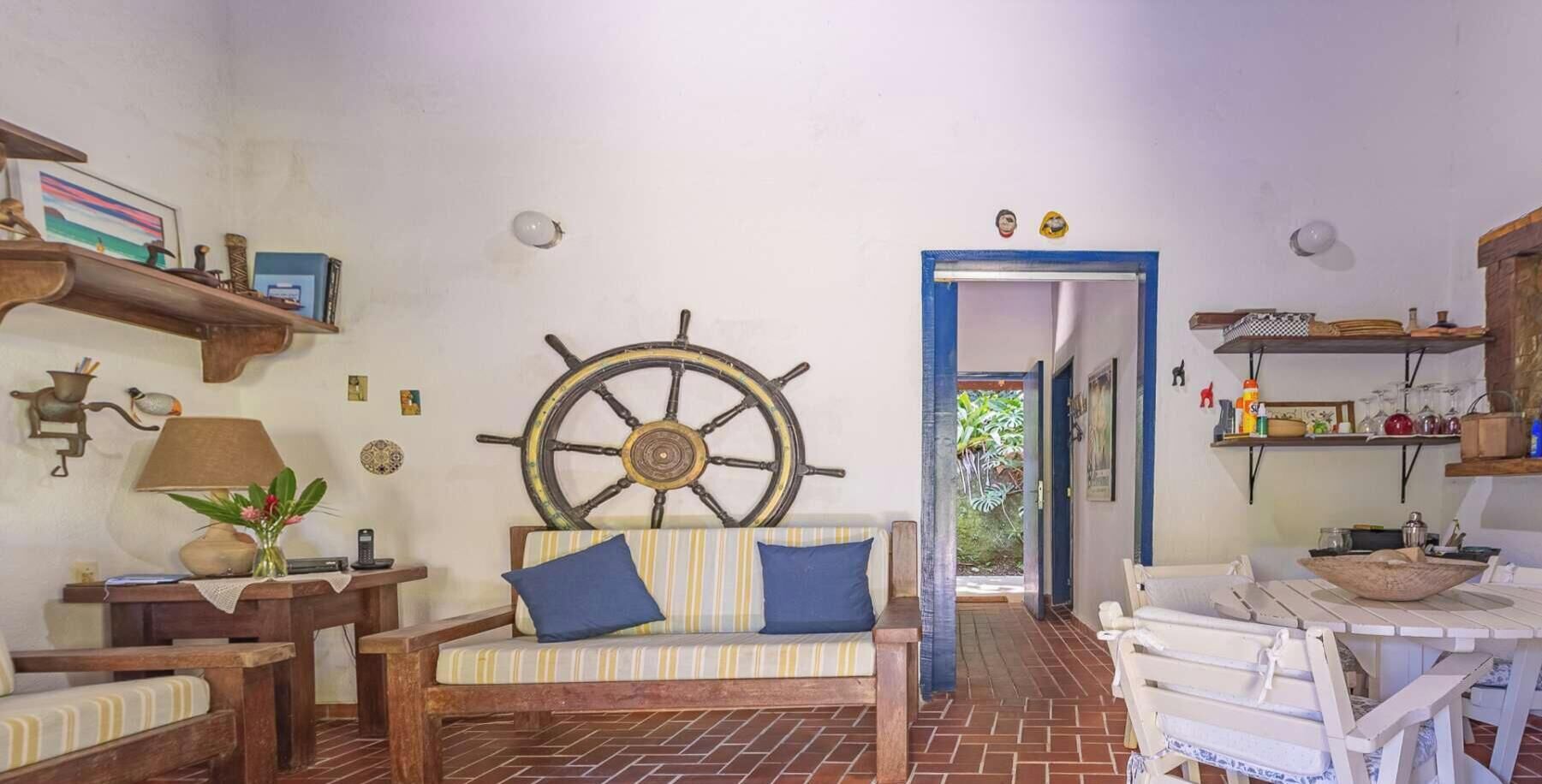 A cozy living room with a wooden sofa, a ship's wheel decoration, and a dining area with a white table and chairs.