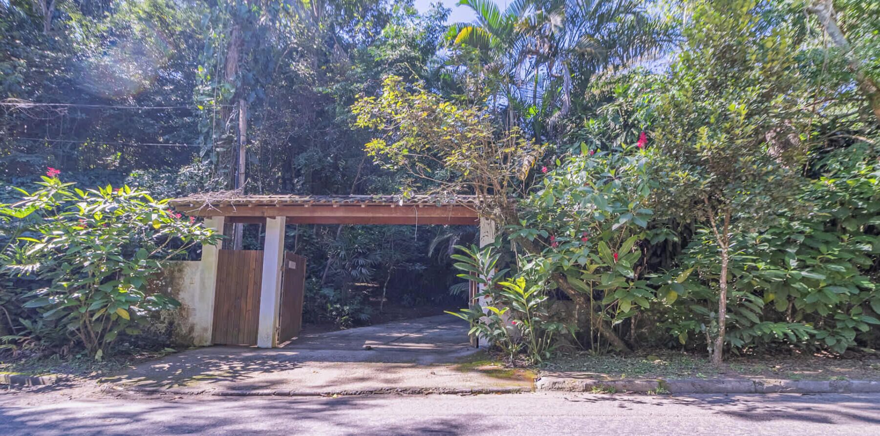 Un sendero serpentea por un jardín con un arco de madera, rodeado de abundante follaje y árboles.