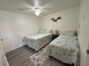 A bedroom with two single beds, a ceiling fan, a nightstand, and a decorative wall piece.