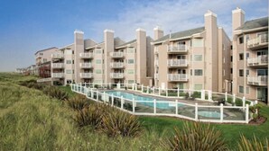 A multi-story residential building with balconies, a swimming pool, and a grassy area. - WM BLOCK Mariners Village 1br (Ocean Shores)