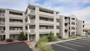 A multi-story residential building with balconies, a parking lot, and a landscaped area with shrubs. - WM BLOCK Mariners Village 1br (Ocean Shores)