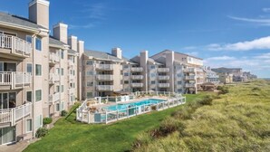 A beachfront hotel with multiple balconies, a swimming pool, and a grassy lawn. - WM BLOCK Mariners Village 1br (Ocean Shores)
