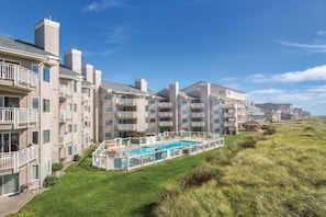 Ein Strandhotel mit mehreren Balkonen, einem Swimmingpool und einer Rasenfläche.