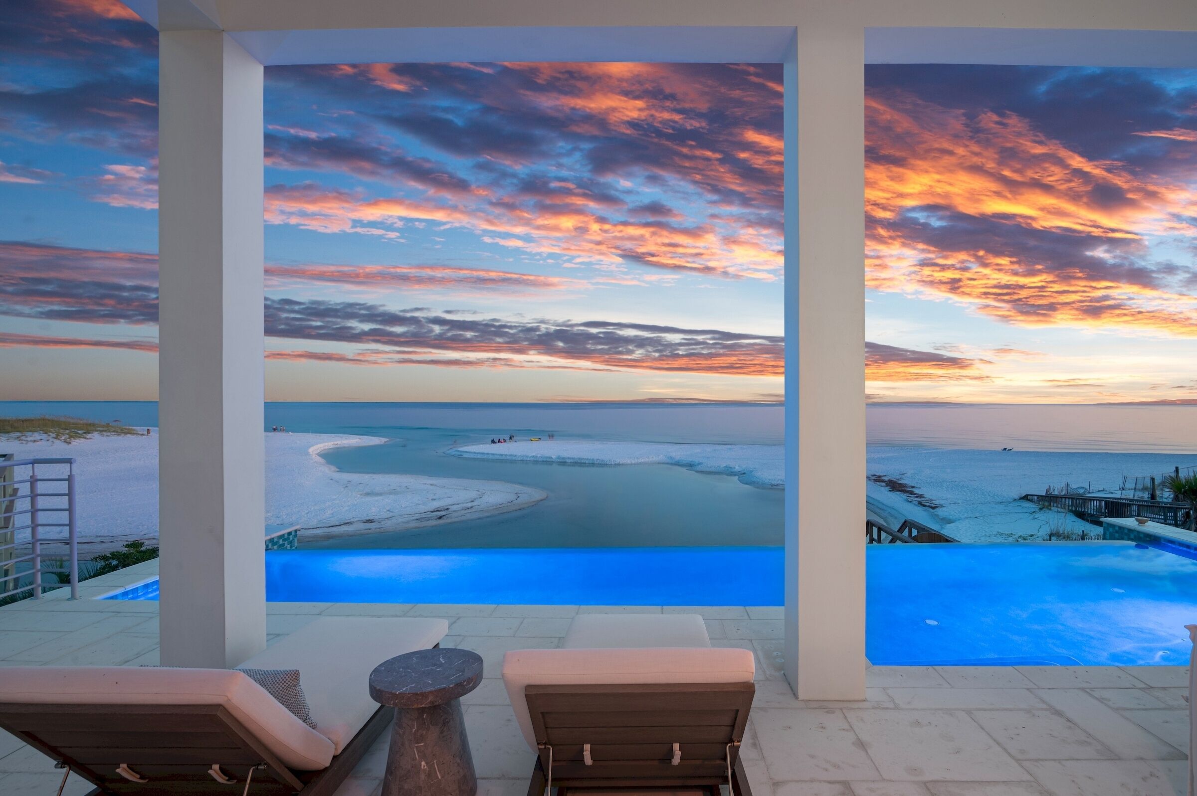A pool area with a view of a beach and sunset.