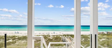 A beach view from a covered area with a wooden deck and white railings.