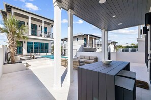 En moderne udendørs terrasse med pool, siddepladser og et overdækket område.