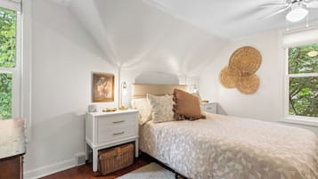 Quarto com cama, mesas de cabeceira, abajur, ventilador de teto e janela com vista para árvores.