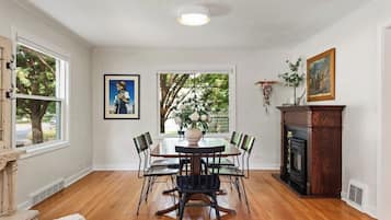 A dining room with a wooden table and chairs, a fireplace, and a window with a view of trees.