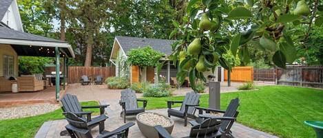 Un patio con sillas Adirondack, una fogata y un árbol con frutos verdes.