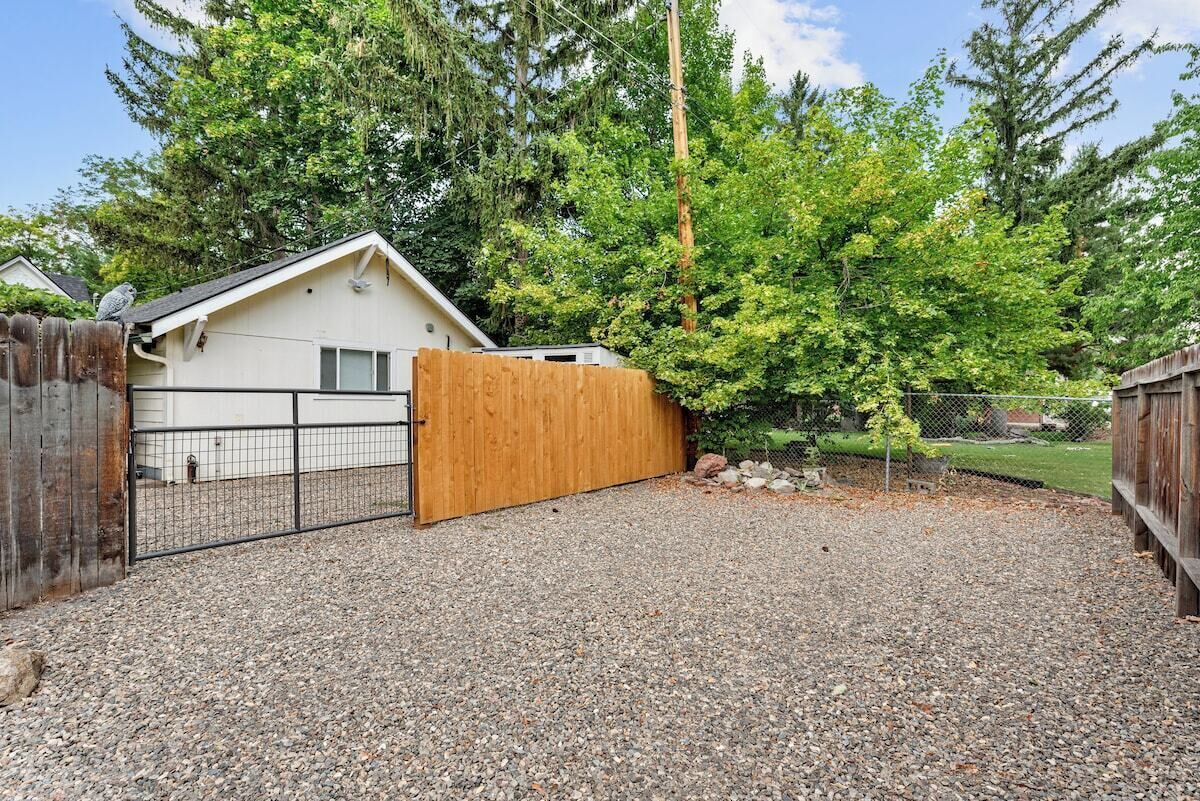 A residential property with a fenced backyard, a wooden gate, and a gravel driveway.