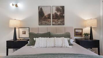A bedroom with a bed, two nightstands, two wall-mounted lamps, two framed pictures, and a potted plant.