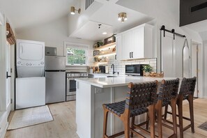 Una cocina moderna con armarios blancos, una isla central y taburetes de bar.