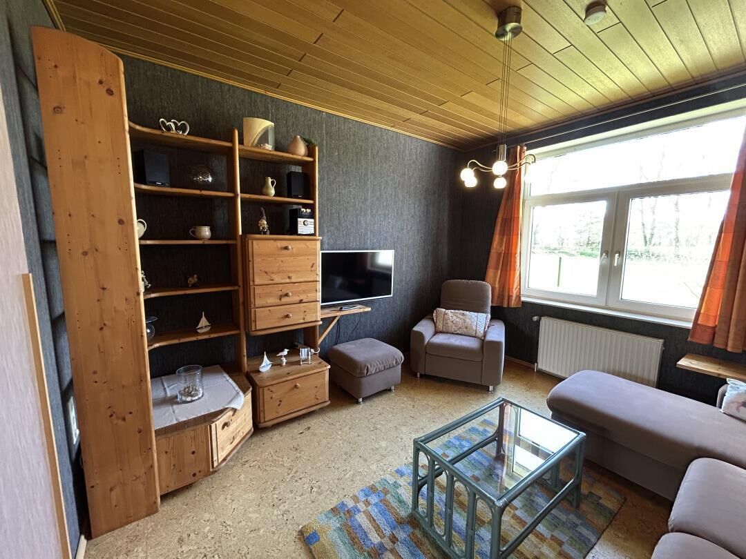 Een woonkamer met televisie, bank, voetenbankje en een houten boekenkast.
