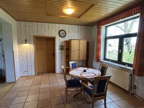 A dining area with a round table, chairs, a clock, and a window with curtains. - NEW! "Ostfriesennest" Vacation Rental (Dunum)