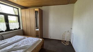 Un dormitorio con cama de madera, una ventana con cortinas, un armario y un radiador.