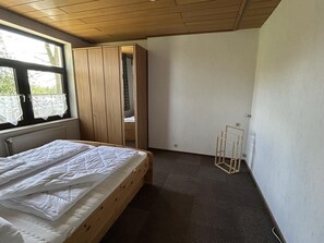 A bedroom with a wooden bed, a window with curtains, a wardrobe, and a radiator. - NEW! "Ostfriesennest" Vacation Rental (Dunum)