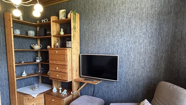Una sala de estar acogedora con televisión, estanterías de madera, un sofá y un pequeño reposapiés.