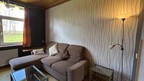 Una sala de estar con un sofá, una mesa de centro de vidrio, una lámpara de pie y un radiador.