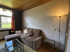 A living room with a sofa, a glass coffee table, a floor lamp, and a radiator. - NEW! "Ostfriesennest" Vacation Rental (Dunum)