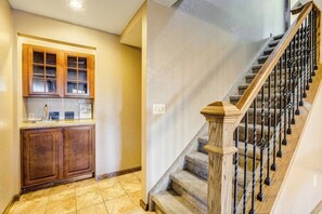 A kitchen with wooden cabinets and a countertop, a staircase with a wooden handrail and metal balusters, and a tiled floor. - 6BR Sleeps 14 · Two Living Areas, Game Room, Hot Tub, Mtn View (Colorado Springs)