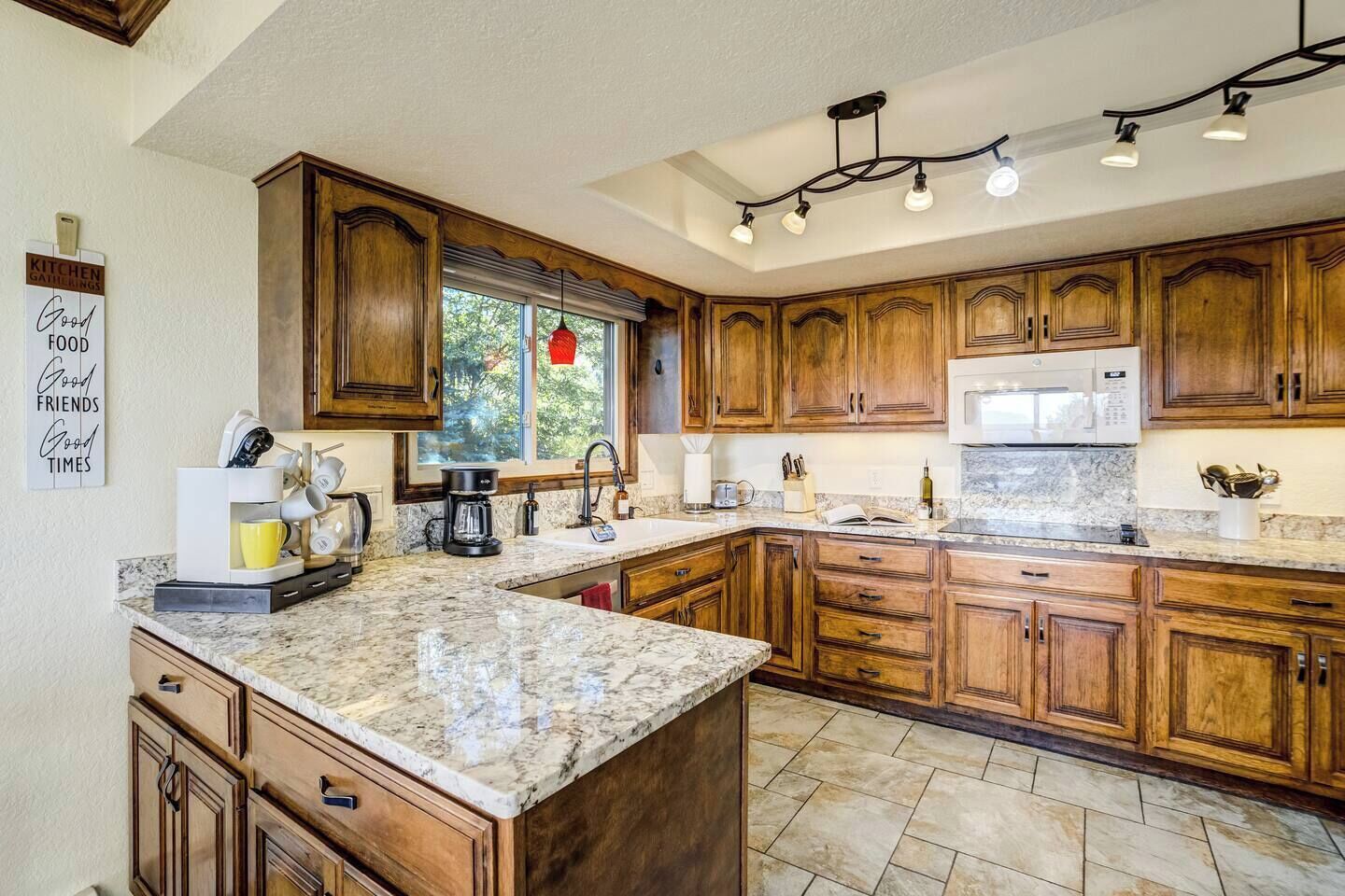 A kitchen with wooden cabinets, a granite countertop, a built-in microwave, and a window with a view of trees.
