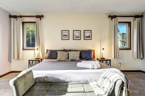 Een slaapkamer met een groot bed, twee nachtkastjes, een stoel en drie ingelijste foto’s aan de muur.