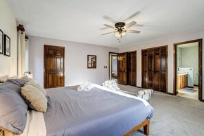 Ein Schlafzimmer mit einem großen Bett, einem Deckenventilator, Holzschränken und einem durch eine offene Tür sichtbaren Badezimmer.