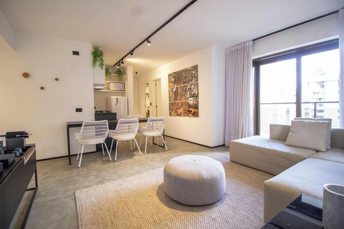 A modern living room with a sofa, ottoman, and a dining area with chairs.