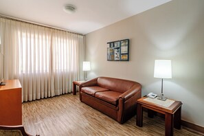 A hotel room with a brown leather sofa, a wooden desk, a lamp, and a painting on the wall. - Classic by Bhomy (São Paulo)