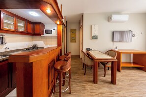 A kitchen with wooden cabinets, a microwave, a gas stove, and a bar area with stools. - Classic by Bhomy (São Paulo)