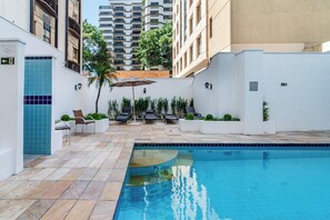 A swimming pool with a tiled deck, surrounded by white walls and a few potted plants. - Classic by Bhomy (São Paulo)