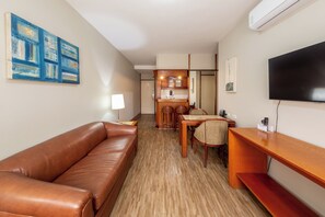A hotel room with a brown leather sofa, a dining table with chairs, a flat-screen TV, and artwork on the walls. - Classic by Bhomy (São Paulo)